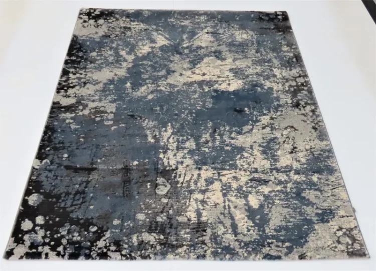 A rug featuring a blend of dark blue and grey colours with a splattered, abstract pattern