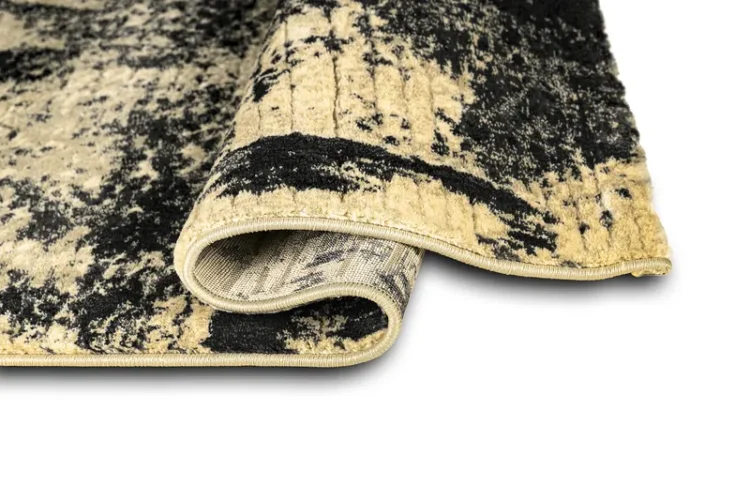 A rug with a cream background with abstract black patterns. The edges are neatly finished, and part of the rug is folded to show the underside